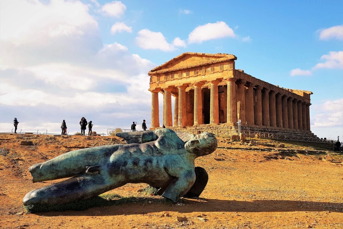 a statue beside a concrete acropolis