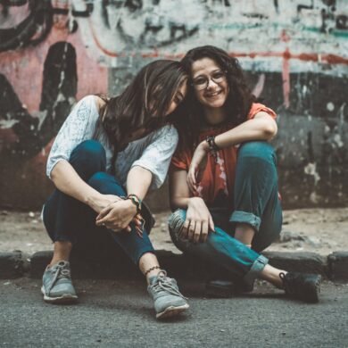two women sitting on pavement near painted wall