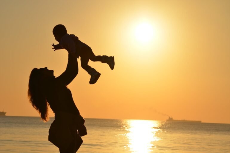 silhouette photo of a mother carrying her baby at beach during golden hour