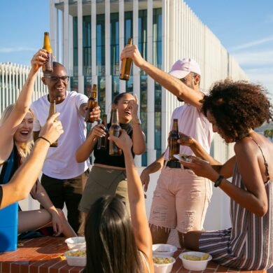 joyful diverse friends toasting with beer bottles on rooftop